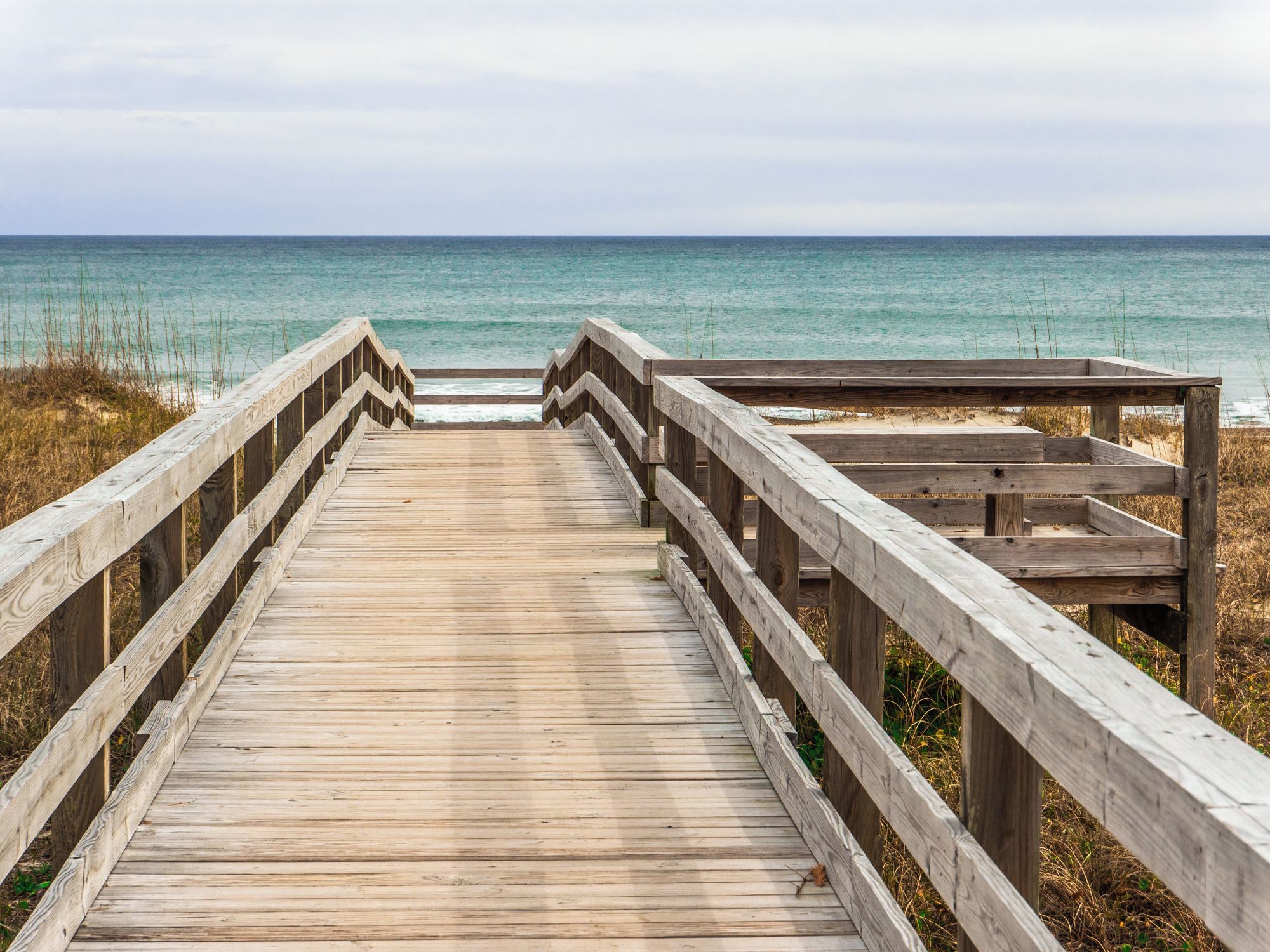 A wooden boardwalk leading to a beach with a clear view of the ocean.