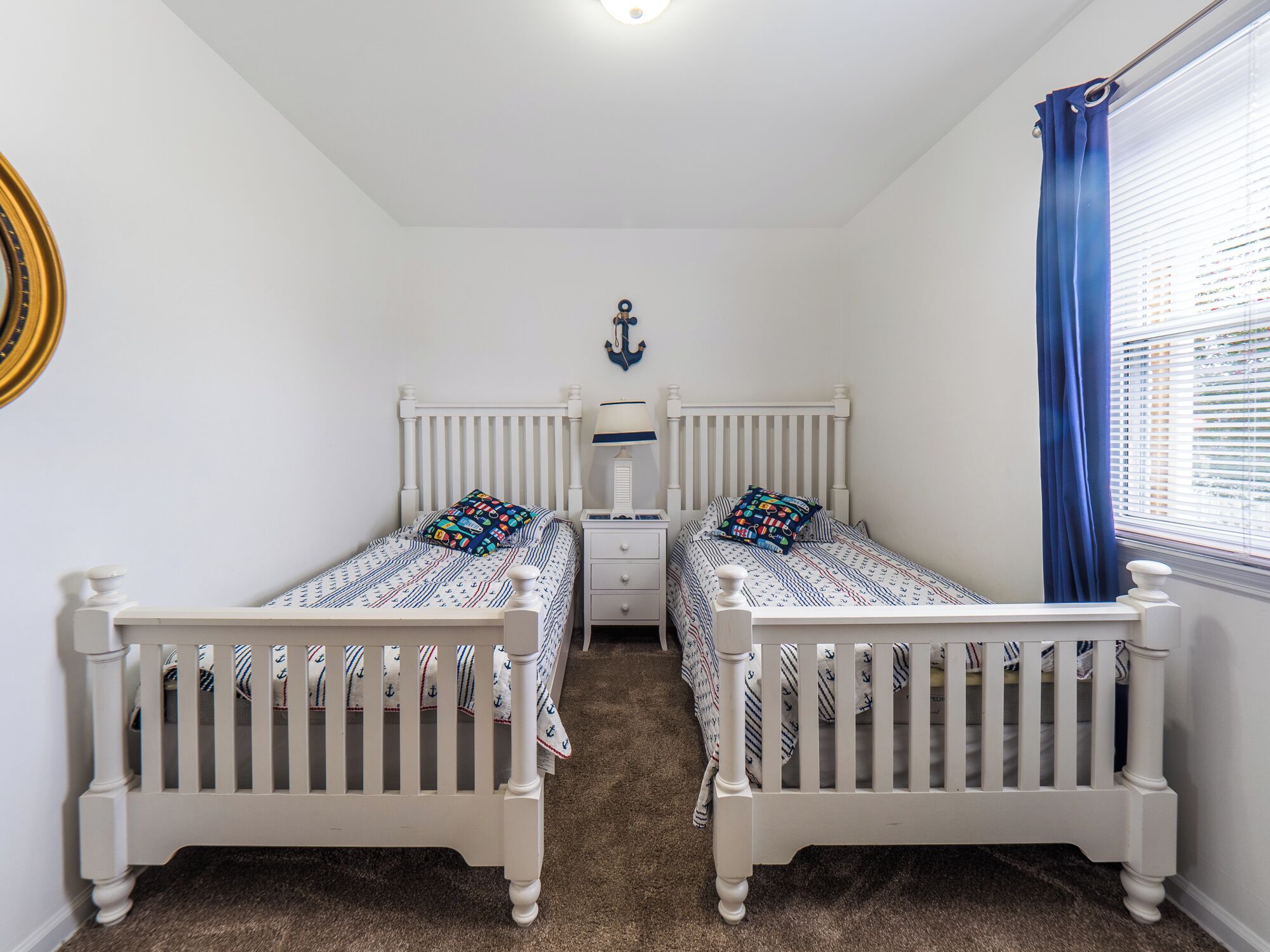 A bedroom with two single beds, a nightstand, a dresser, and a window with blue curtains.
