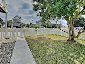 A residential area with a white picket fence, a tree, and a building with a balcony. - Dooley's Place by Carolina Retreats (Carolina Beach)