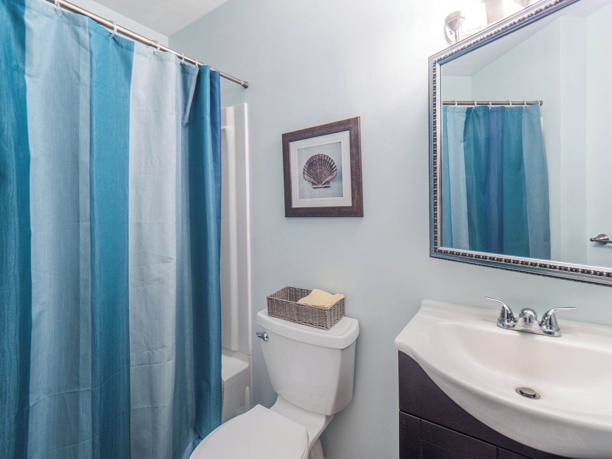 A bathroom with a white toilet, a sink with a mirror, and blue shower curtains.