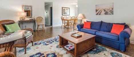 A living room with a blue sofa, wooden coffee table, wicker chairs, and a patterned rug.