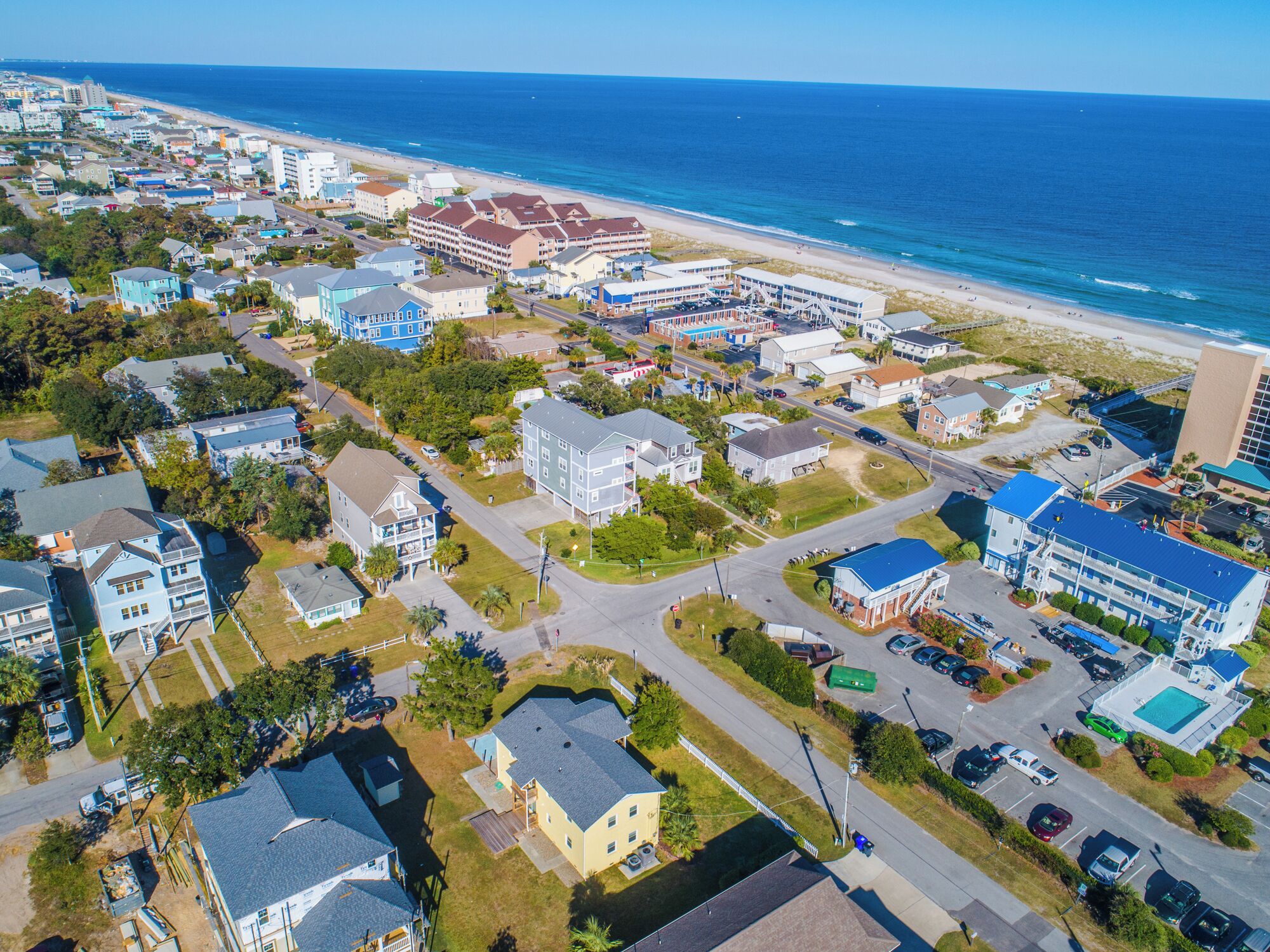 Vista aérea de un pueblo costero con un hotel frente a la playa, edificios residenciales y una vista despejada del océano.