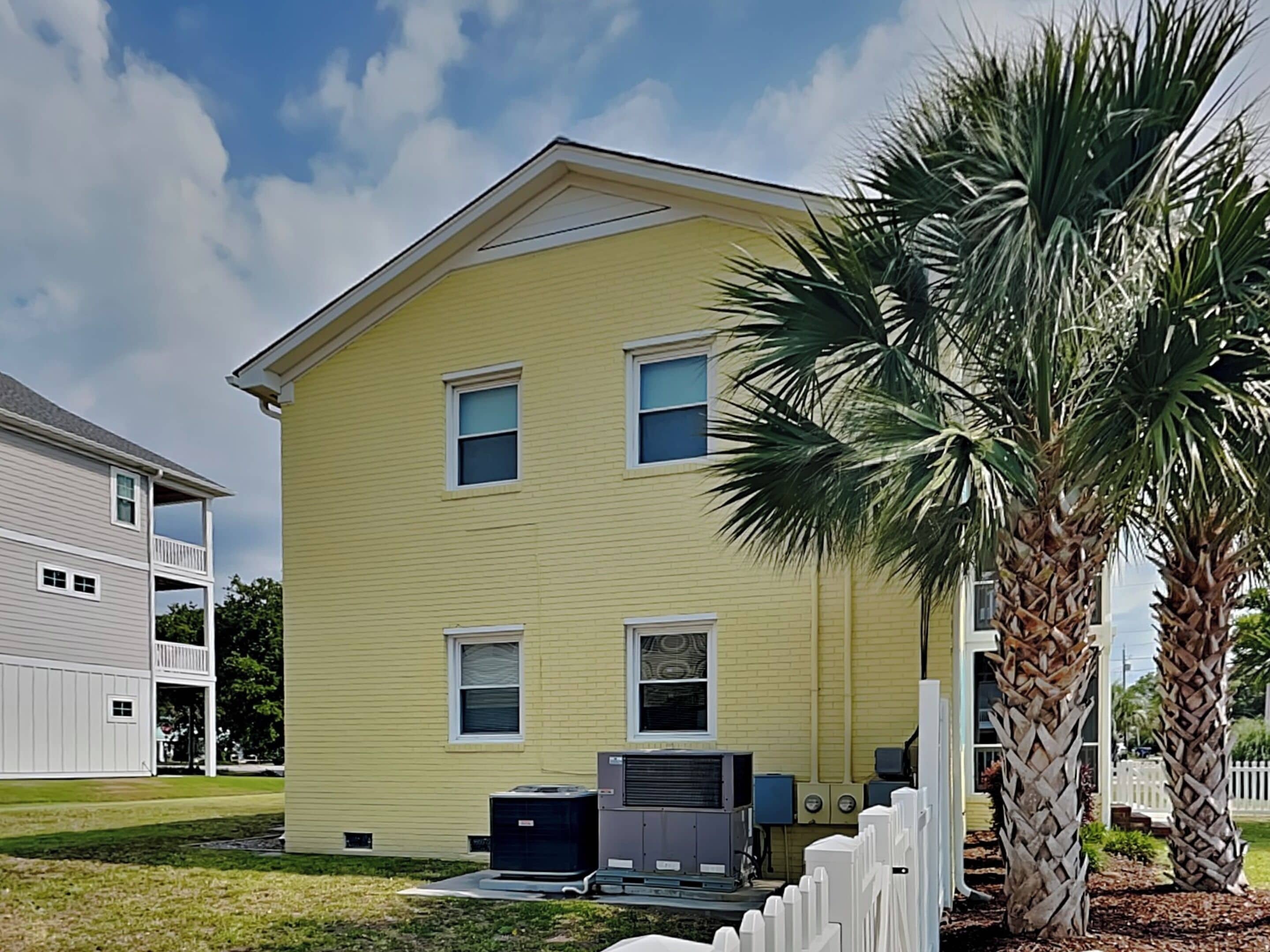 A two-story yellow house with a white porch and a palm tree in the front yard.