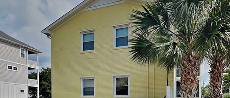 A two-story yellow house with a white porch and a palm tree in the front yard.