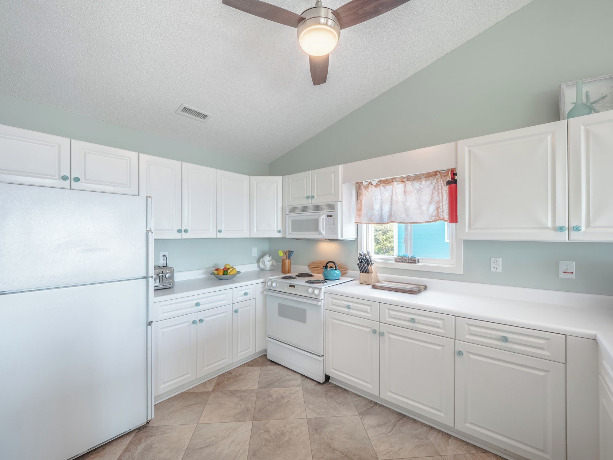 A kitchen with white cabinets, a microwave, a stove, and a ceiling fan.