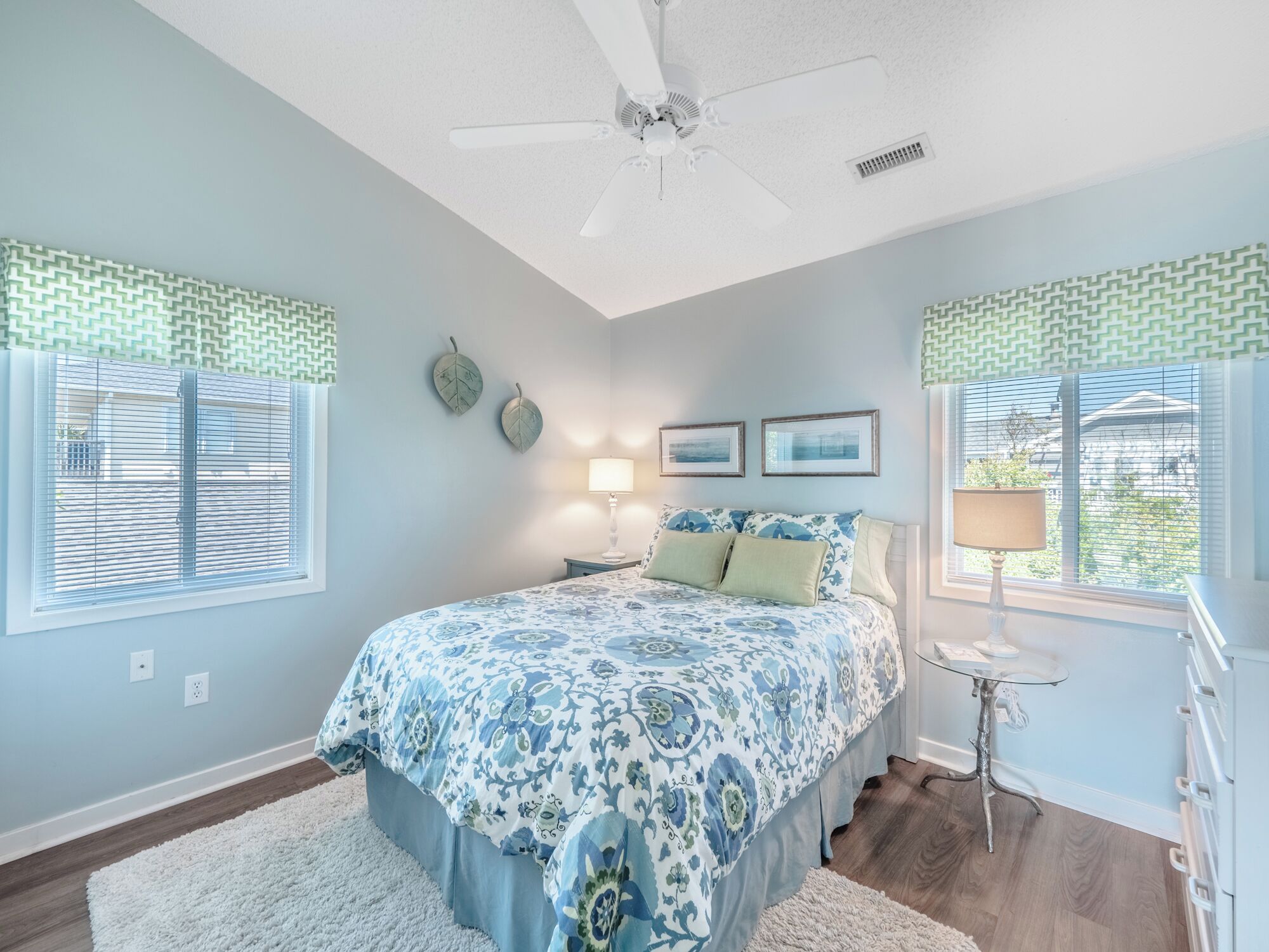 A bedroom with a bed, a ceiling fan, two wall-mounted lamps, and a window with blinds.