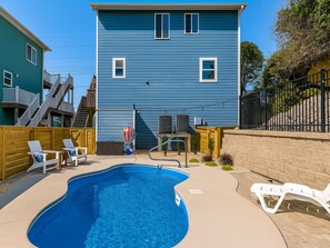 A backyard with a swimming pool, a wooden deck, and a blue house with white windows. - Blue Haven by Topsail Realty (Holly Ridge)