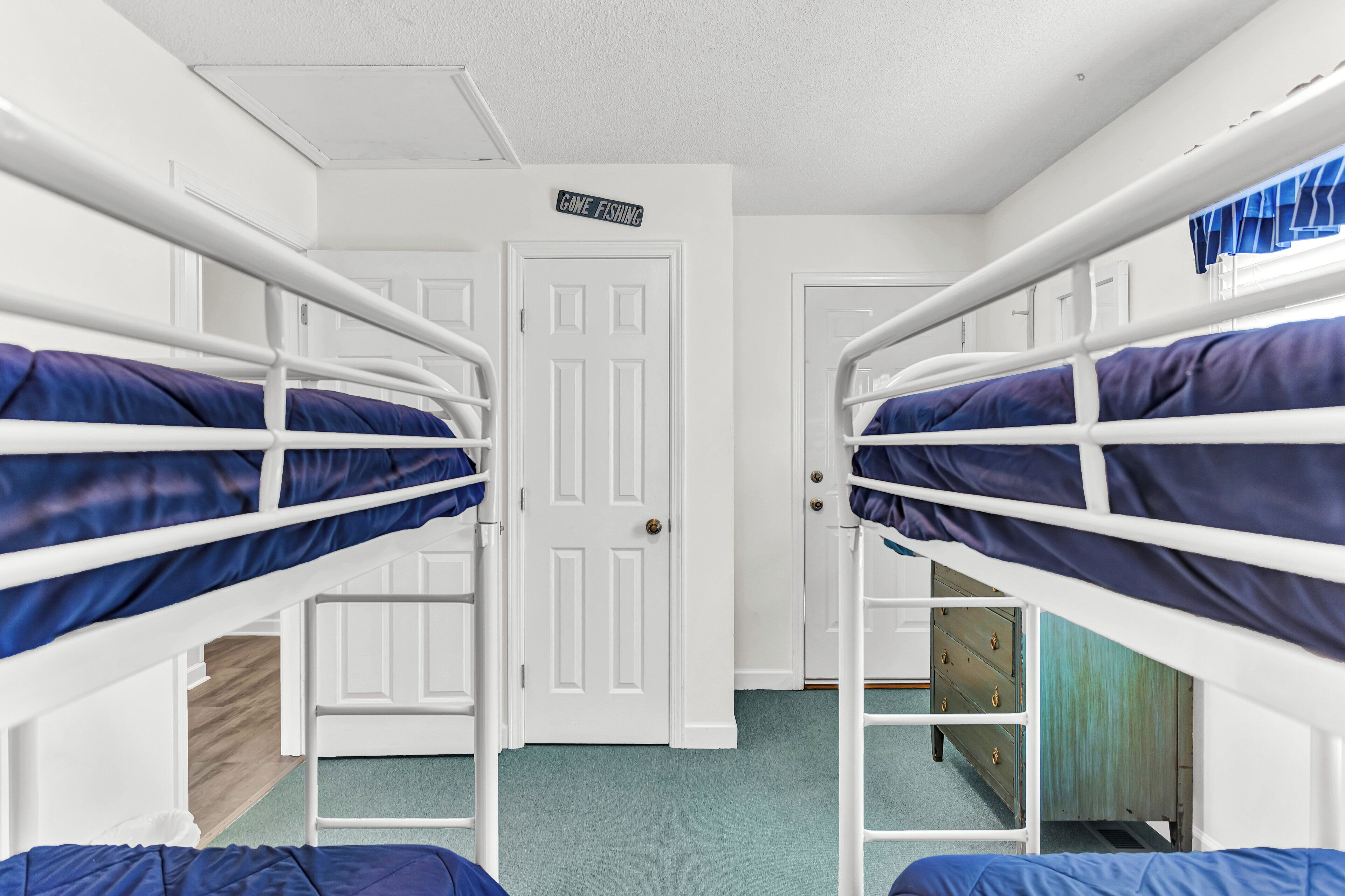 Une chambre de dortoir avec des lits superposés, une porte sur laquelle est écrit « Je suis parti pêcher » et une petite commode.
