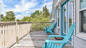 A wooden deck with two turquoise Adirondack chairs, a white railing, and a view of trees and a house with blue shutters. - Just Beachy Spartanburg by Carolina Retreats (Carolina Beach)