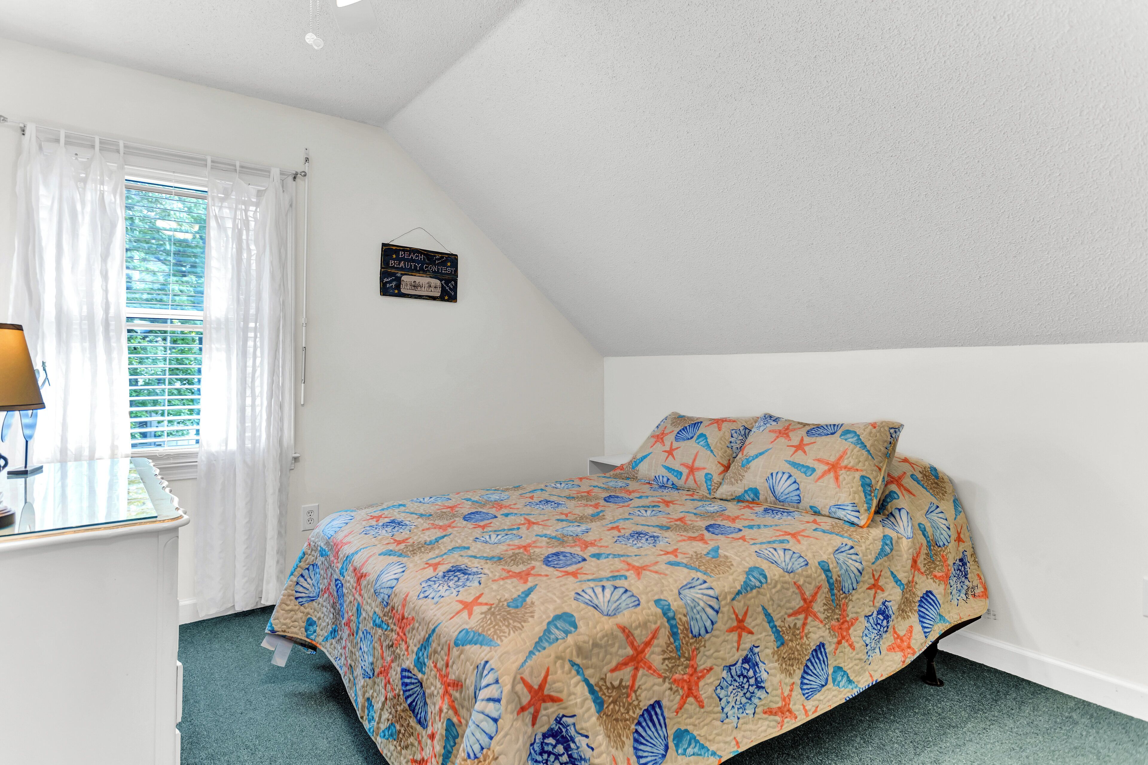 A bedroom with a bed, a desk, and a window with curtains.