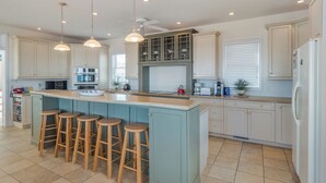 A modern kitchen with a central island, bar stools, and a ceiling fan. - Over The Moon by Carolina Retreats (Kure Beach)