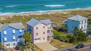 A coastal residential area with houses near the beach, including a blue house with a balcony and a pink house with a garage. - Over The Moon by Carolina Retreats (Kure Beach)