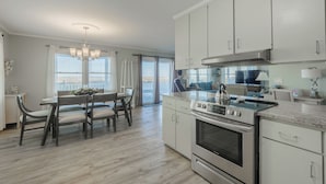 A modern kitchen with white cabinets, a large stove, and a dining area with a table and chairs. - Seaship by Carolina Retreats (Carolina Beach)