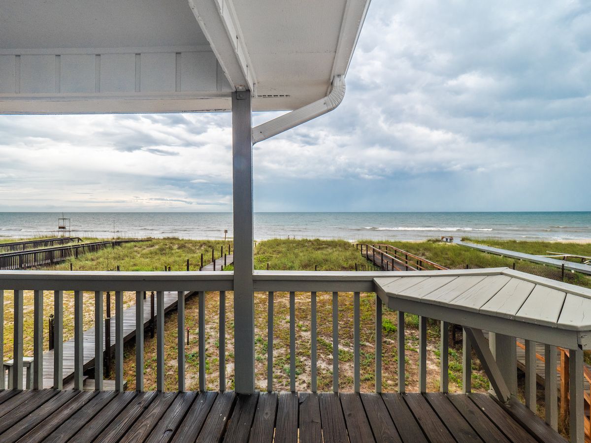 A wooden deck with a railing overlooking a beach and ocean.