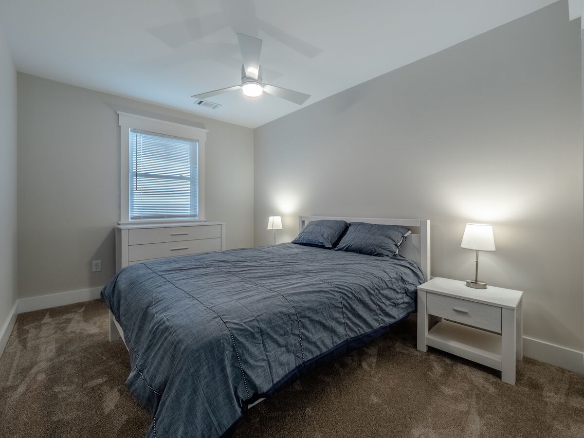 A bedroom with a bed, two bedside tables, a ceiling fan, and a window with blinds.