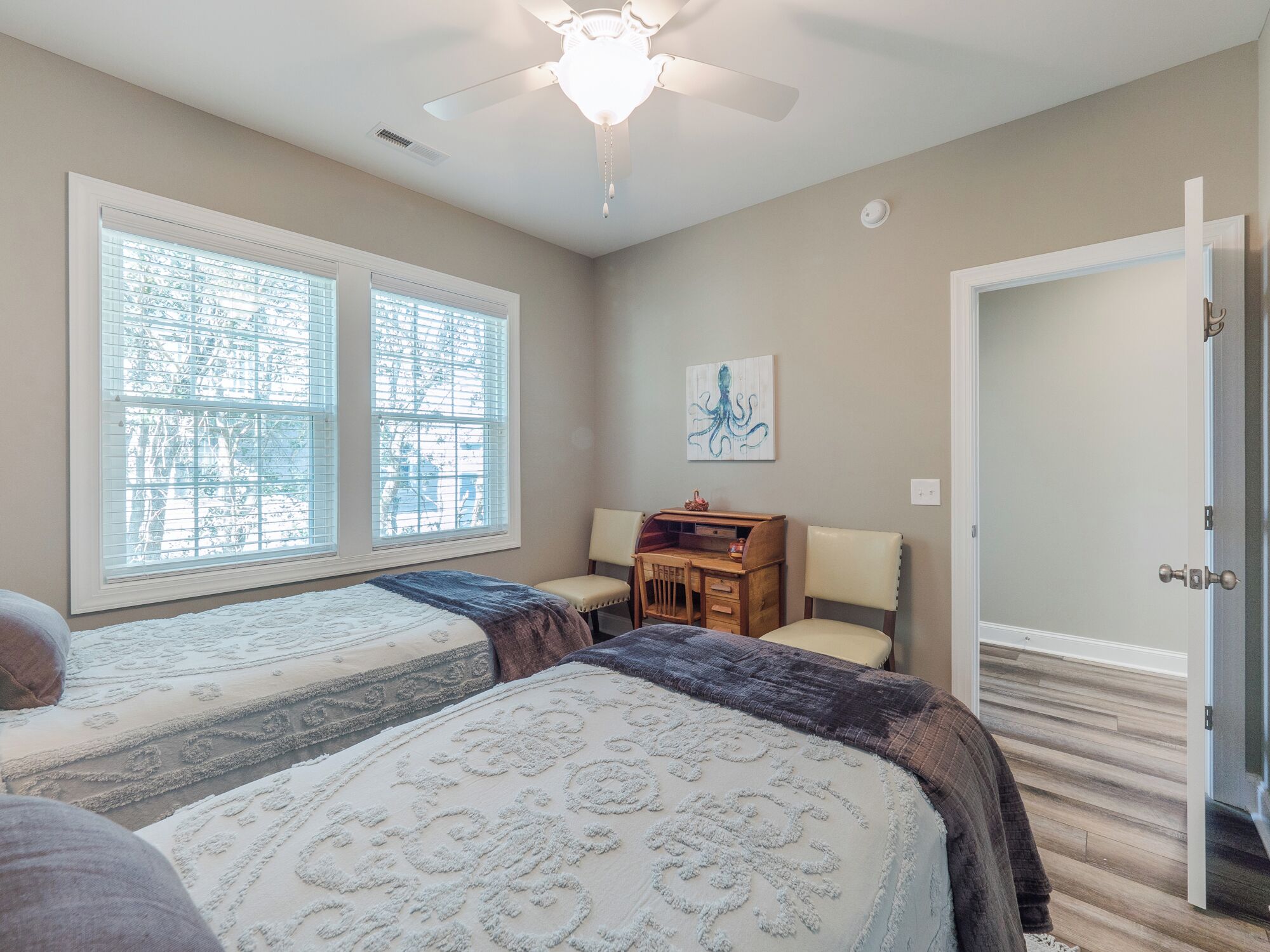 A bedroom with two beds, a desk, and a ceiling fan.
