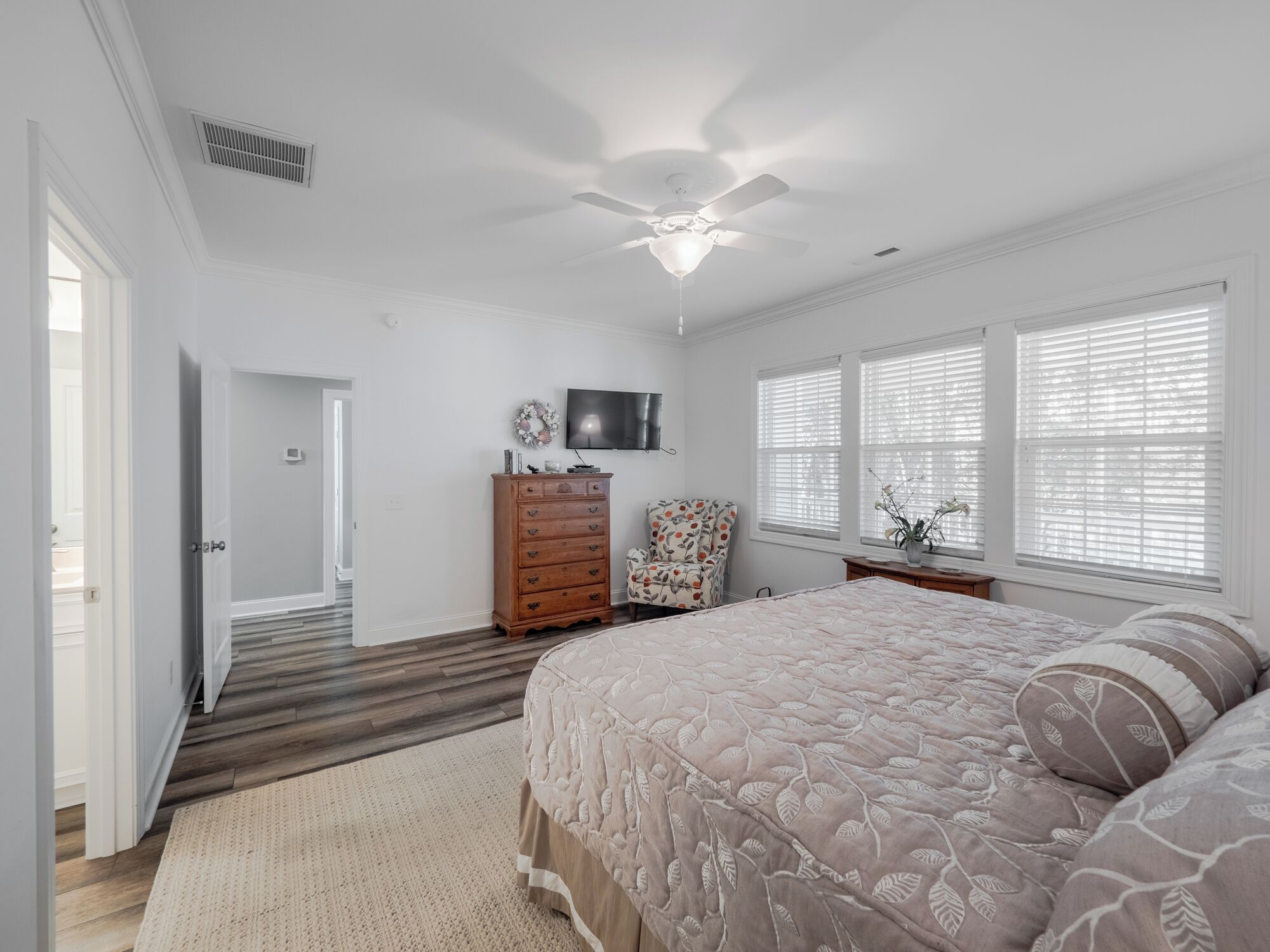 Un dormitorio con cama, cómoda, silla y televisor en la pared.