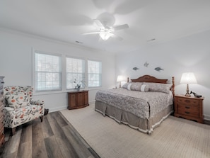 A bedroom with a bed, two bedside tables, a chair, and a ceiling fan. - A Kure Cure by Topsail Realty (Kure Beach)