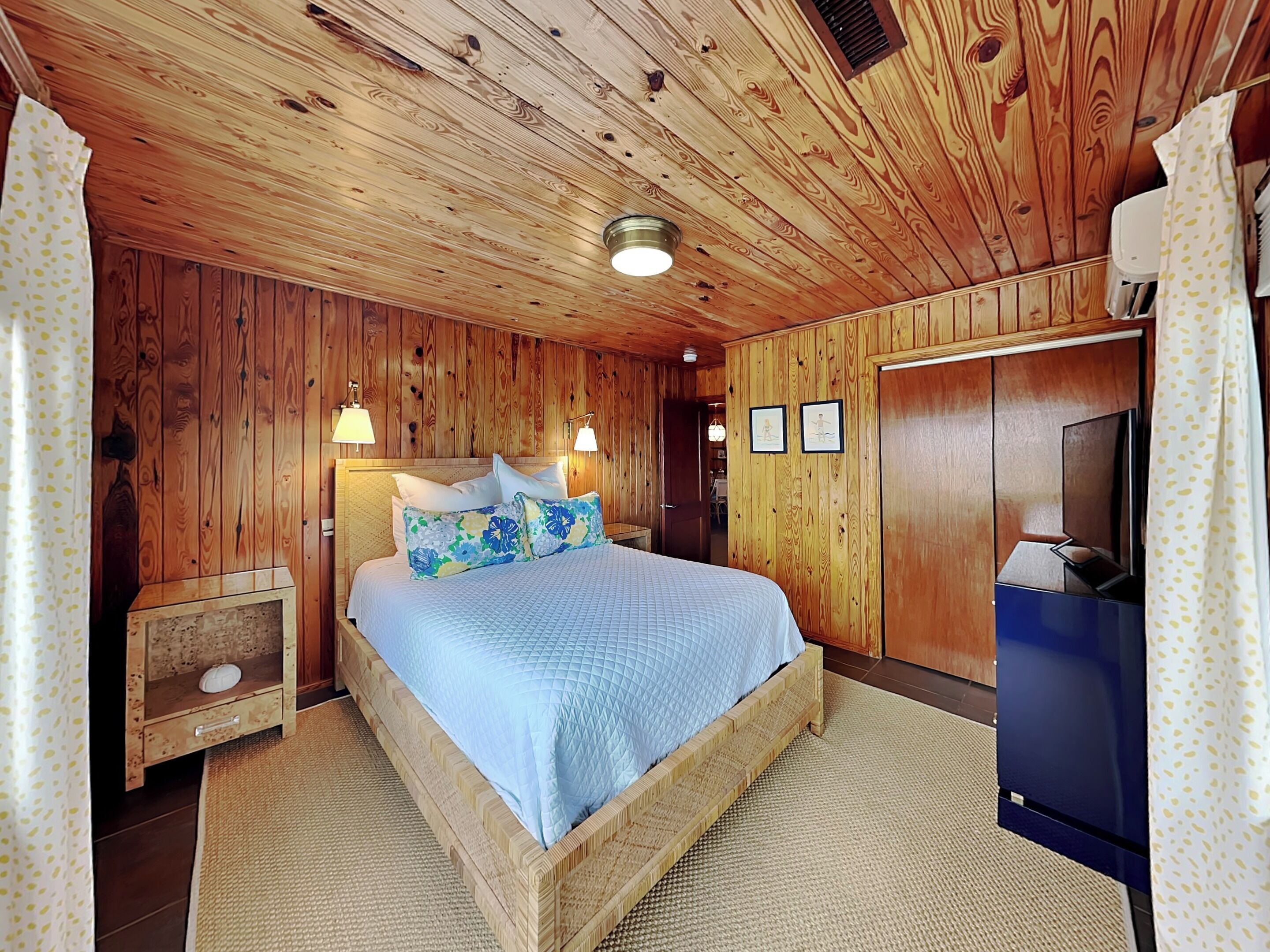 Een kamer met houten lambrisering, een bed, nachtkastjes, een televisie en een kledingkast.