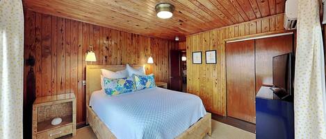 Een kamer met houten lambrisering, een bed, nachtkastjes, een televisie en een kledingkast.