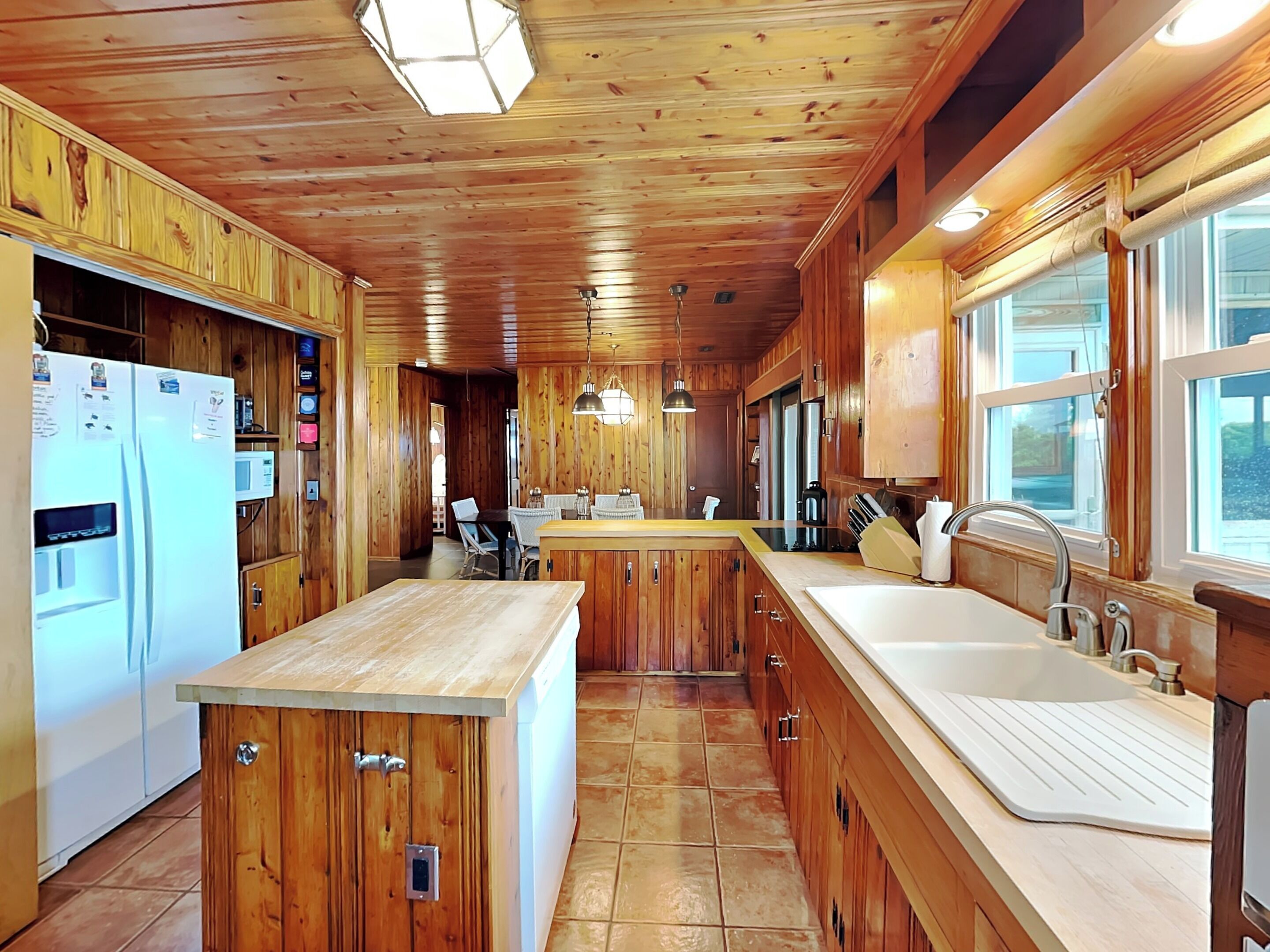 A wooden cabin interior with a kitchen, dining area, and a large window.