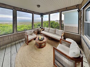 A sunroom with large windows, a wooden floor, and a sectional sofa.