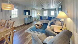 Un salón amplio con un sofá grande, una mesa de centro y un televisor. Hay una zona de comedor con sillas y una mesa.