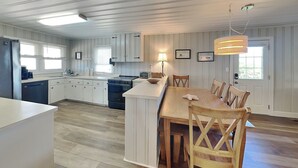 Una cocina moderna con armarios blancos, una mesa de comedor de madera y una lámpara colgante.