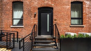 A brick building with a black door, a staircase with black railings, and windows with white curtains.
