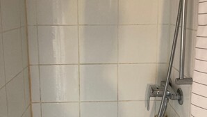 Douche met een handdouche en een flexibele slang, bevestigd aan een betegelde muur.