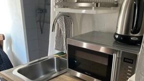 Een kleine keuken met een roestvrijstalen spoelbak, een magnetron en een waterkoker.