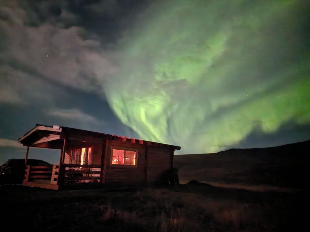 Eine Holzjagdhaus mit Veranda, unter einem Nachthimmel mit grünem Polarlicht.