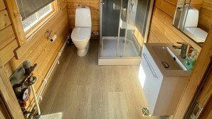 Baño de una cabaña de madera compacta, con inodoro, ducha y lavabo.