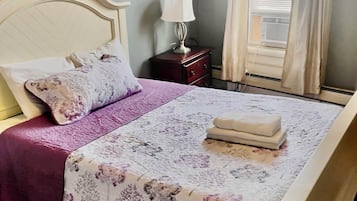 A neatly made bed with a floral bedspread, a bedside lamp, and a window with curtains.