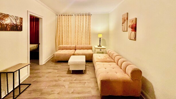 Una sala de estar con sofá, reposapiés y una lámpara sobre una mesita.