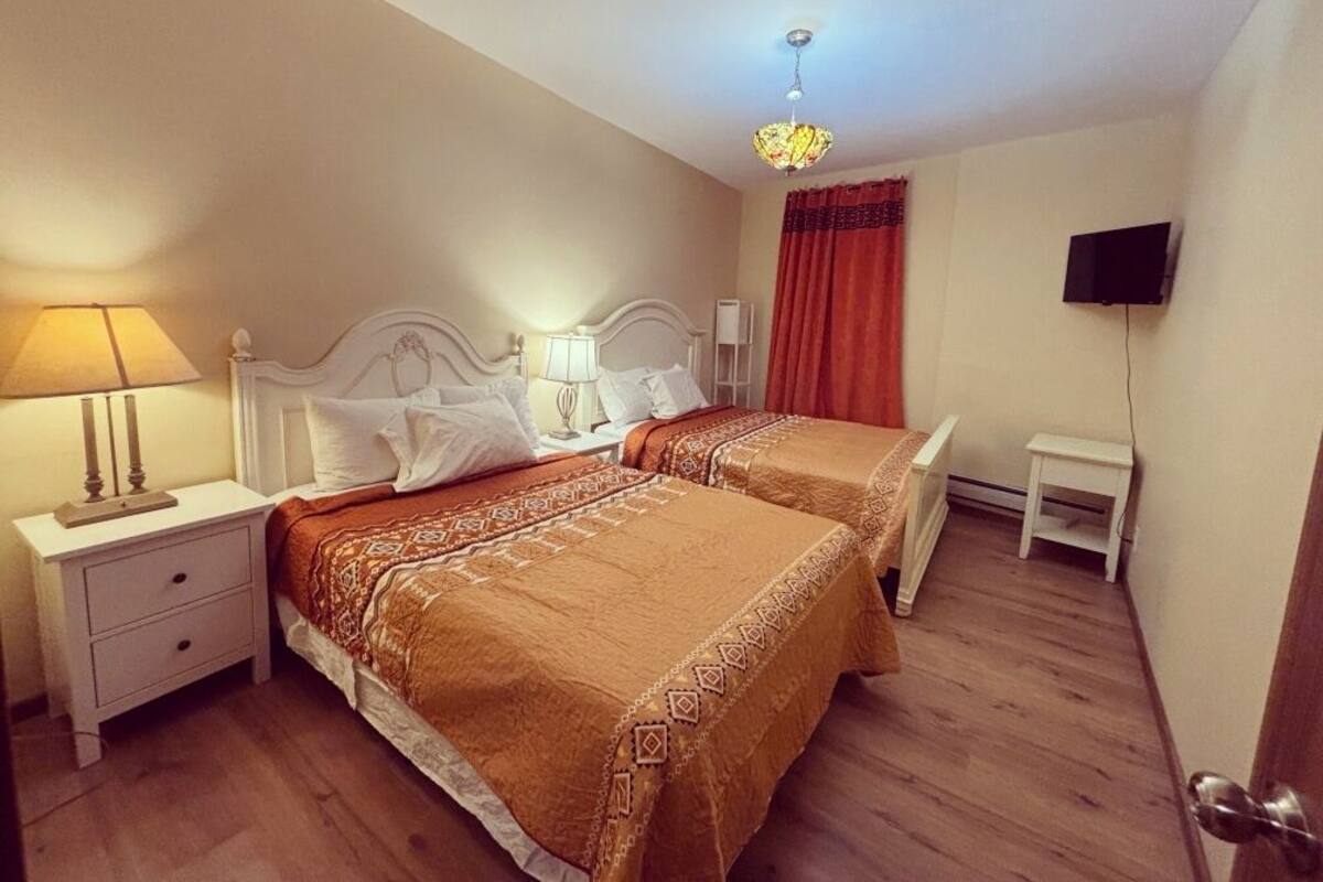 Une chambre d’hôtel avec deux lits, une table de chevet avec une lampe, une petite table et un téléviseur fixé au mur.