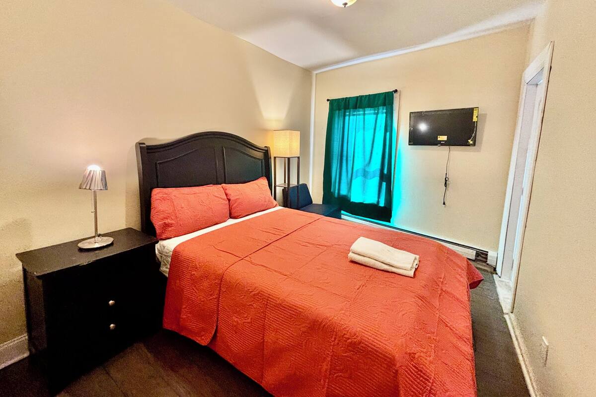 Une chambre d’hôtel avec un lit, une table de chevet, une lampe, une télévision et une fenêtre avec des rideaux.