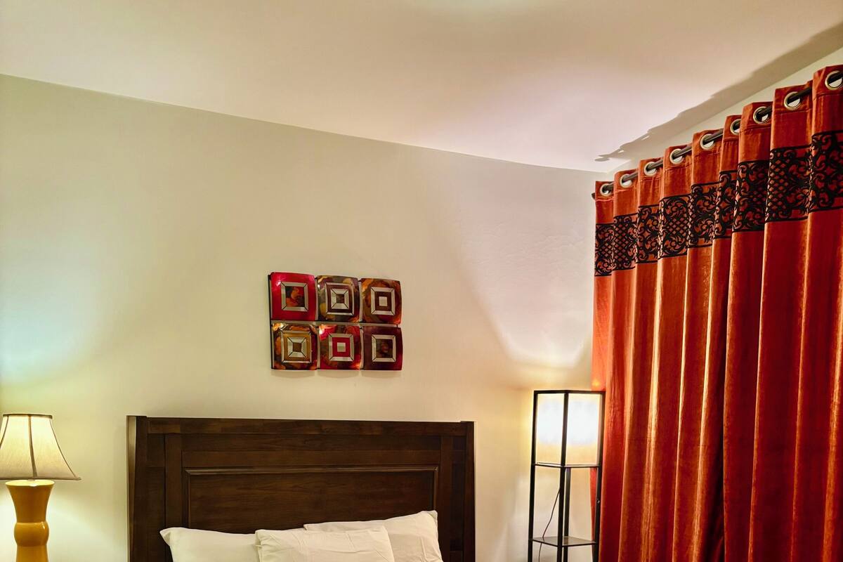 Un lit bien fait, avec une couvre-lit à motifs, une tête de lit en bois et une table de chevet sur laquelle se trouve une lampe.
