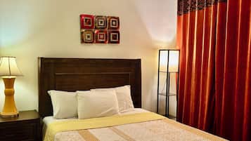 A neatly made bed with a patterned bedspread, a wooden headboard, and a bedside table with a lamp.