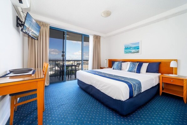 Une chambre d’hôtel avec un grand lit, un bureau, une chaise, un téléviseur fixé au mur et un balcon donnant sur la mer.