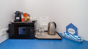 Een kitchenette met een magnetron, koffiezetapparaat en waterkoker op een blauw aanrecht.