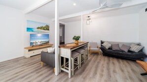 A modern living room with a sofa, a dining area with a wooden table and chairs, and a television displaying a holiday message.