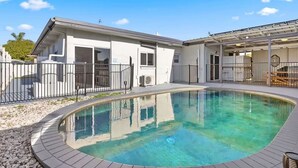 A pool area with a clear blue pool, a covered patio, and a building with a white exterior and large windows.
