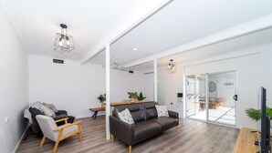 A modern living room with a dark leather sofa, a wooden chair, and a dining area with a table and chairs.