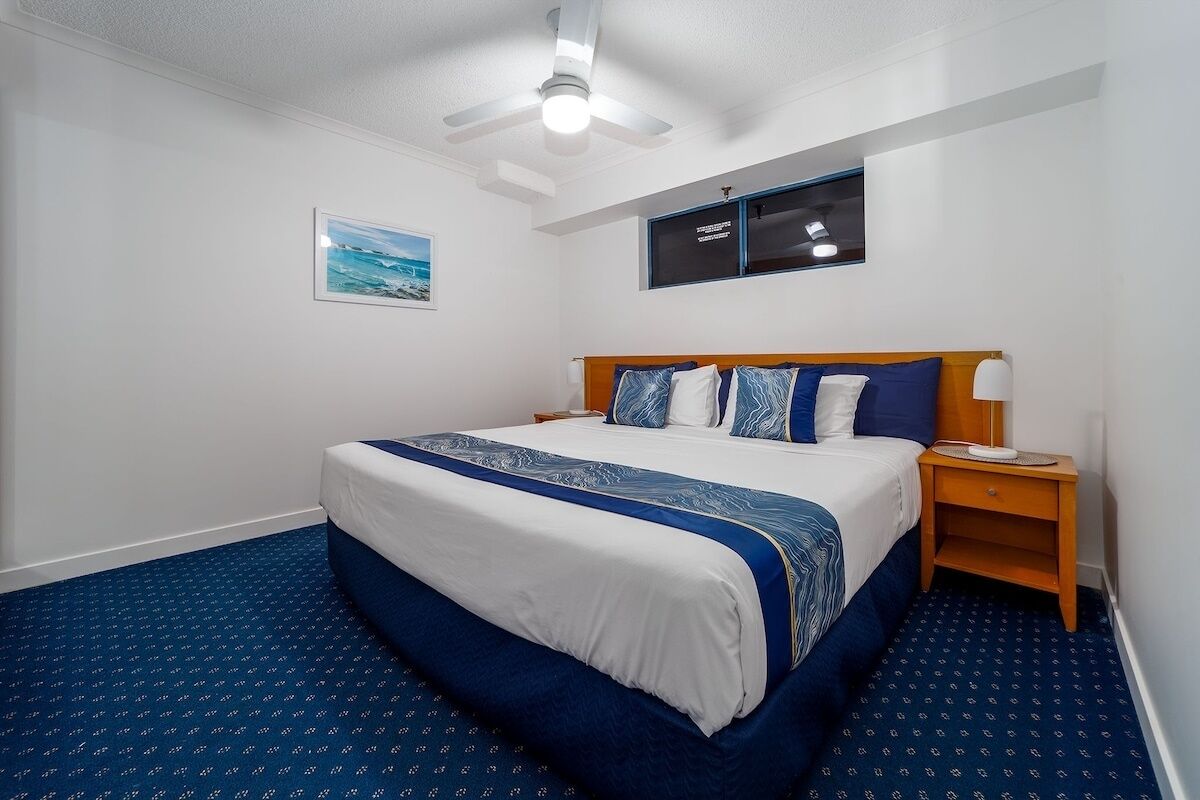 Una habitación de hotel con una cama grande, un ventilador de techo, una mesita de noche y un cuadro en la pared.