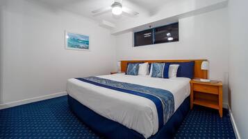 Una habitación de hotel con una cama grande, un ventilador de techo, una mesita de noche y un cuadro en la pared.