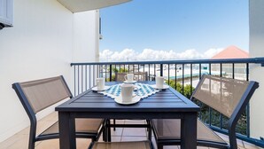 Un balcón con una mesa dispuesta para cuatro, sillas y vistas al mar y edificios.