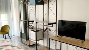 Een moderne kamer met een televisie op een houten standaard, een hoge kast met kleding en een kamerkleed met een patroon.