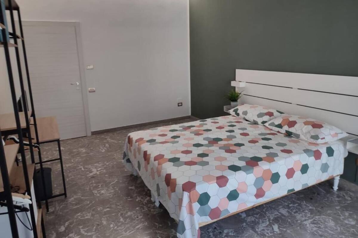 A bedroom with a bed, a white headboard, a grey wall, and a door.