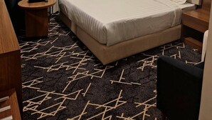 A hotel room with a bed, a chair, a nightstand, a lamp, and a window with curtains. - Wahat Al Madinah Hotel Apartments (Madinah)
